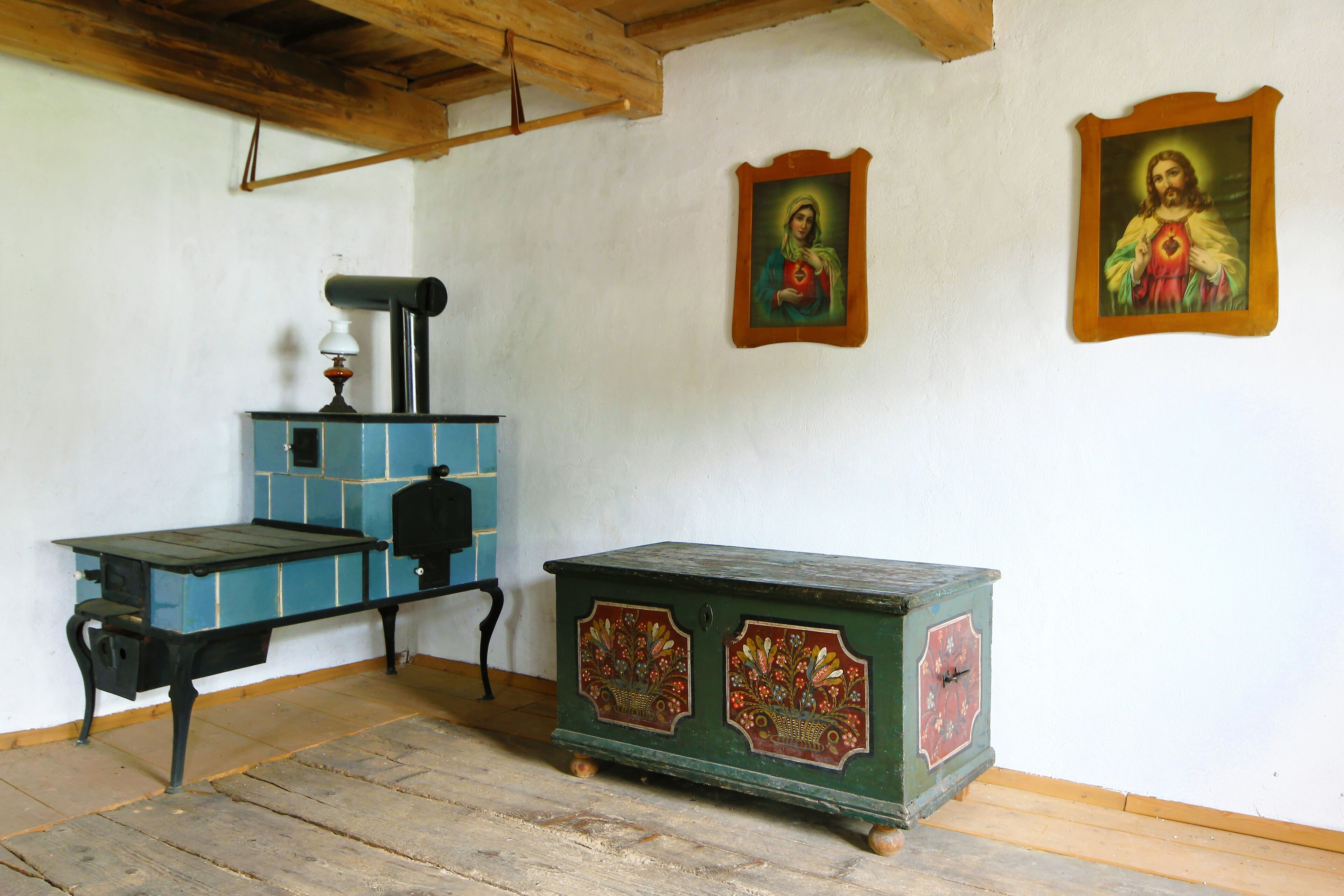Una habitación con una mesa de madera, un aparador verde con diseños florales y dos cuadros religiosos en la pared.