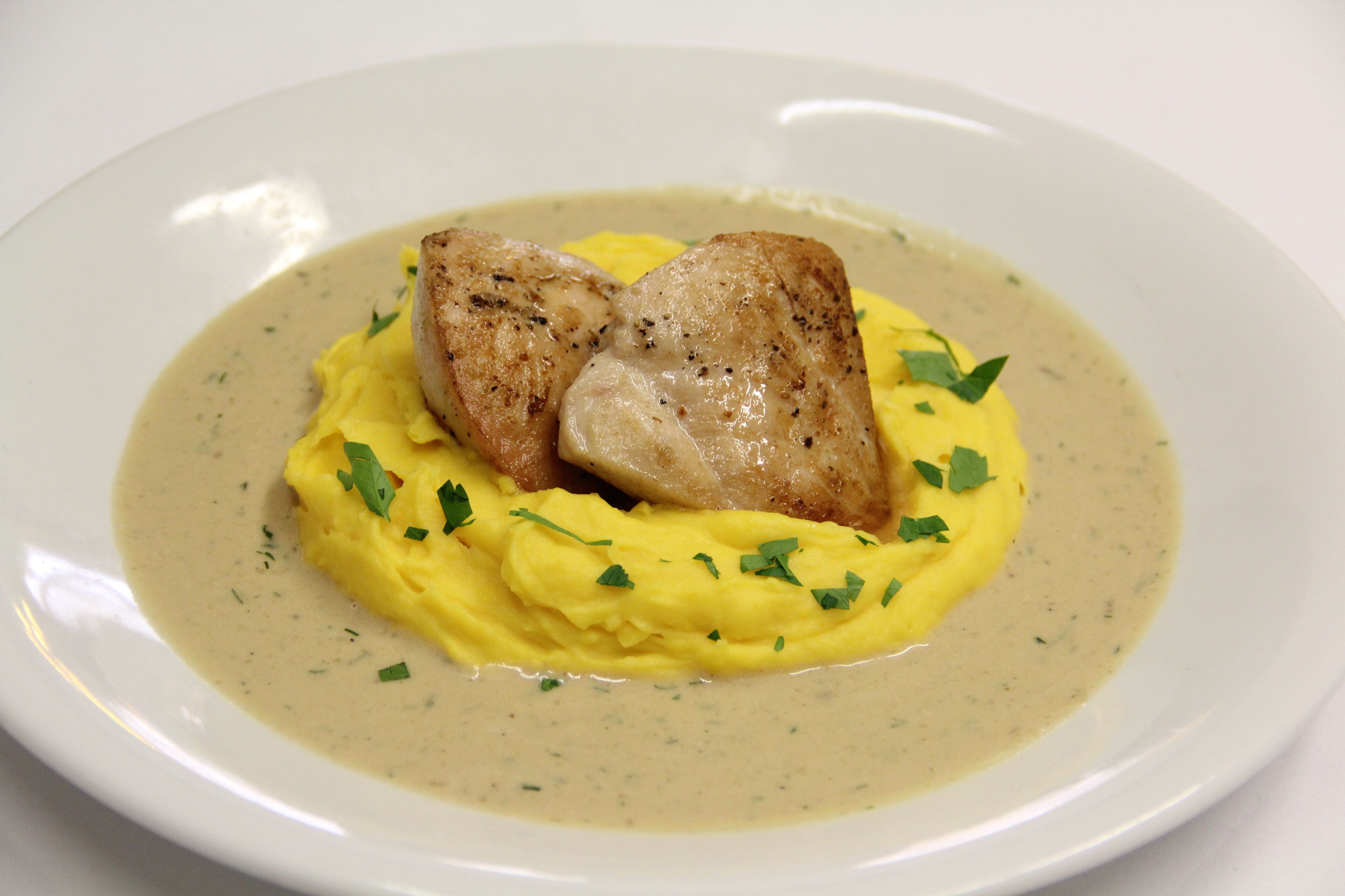 A plate of food with mashed potatoes and a creamy sauce, garnished with herbs.