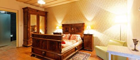 Ein Schlafzimmer mit einem hölzernen Bett, zwei Nachttischen mit Lampen, einem Sessel und einem kleinen Tisch mit einem Kandelaber.