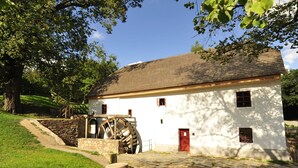 A white building with a red door and windows, a large water wheel, and a stone pathway.