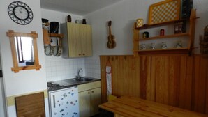 Une cuisine compacte avec des meubles de rangement en bois, un petit réfrigérateur, une table en bois et une étagère à carreaux.