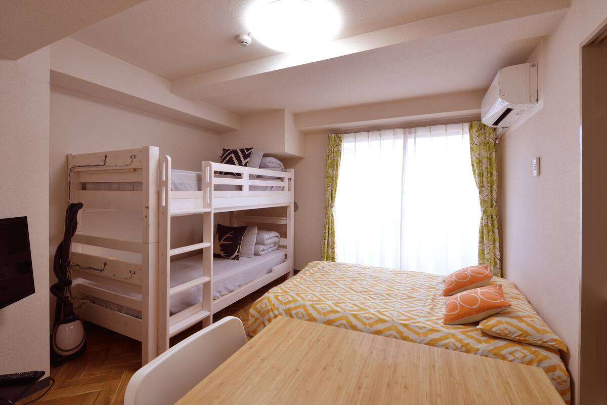 A bunk bed with a desk and chair, a bed with patterned bedding, and a window with curtains.