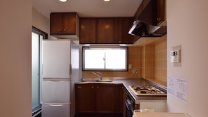 A compact kitchen with wooden cabinets, a built-in oven, a sink, and a window providing natural light. - Hostel Inn Tokyo Kuramae (Tokyo)