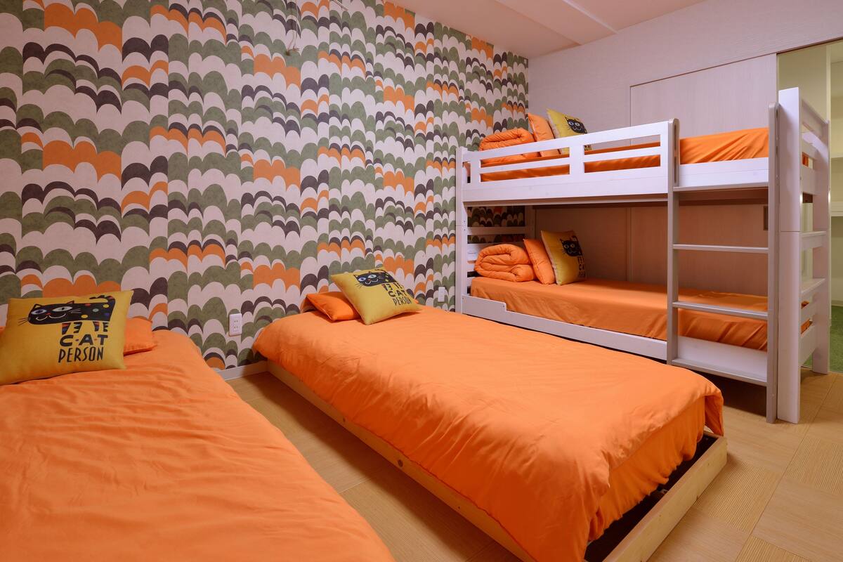 A room with two single beds and a bunk bed, all with orange bedding.