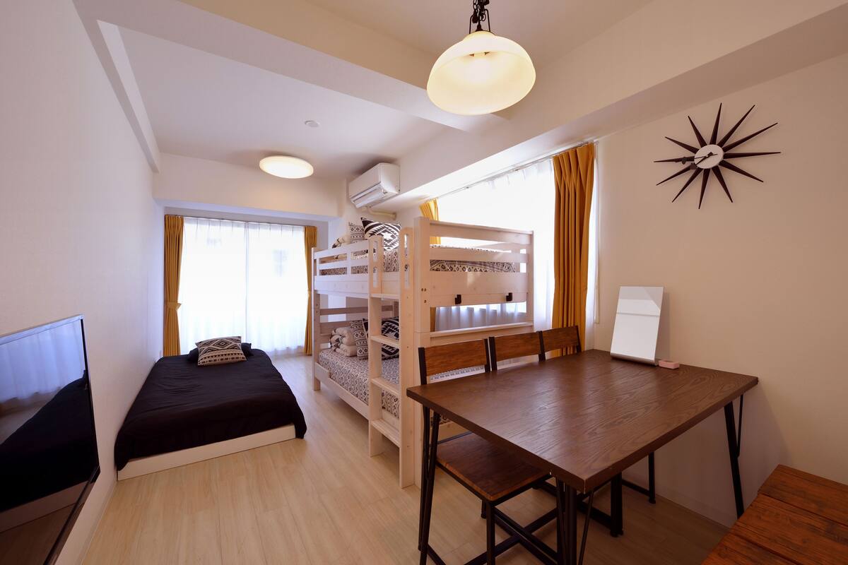 A room with a bunk bed, a desk, a chair, a TV, and a ceiling light.