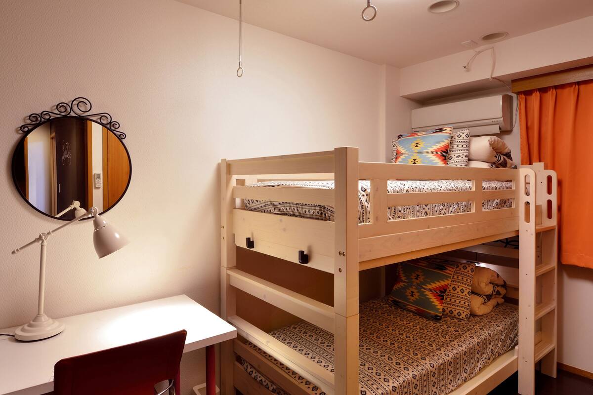 A bunk bed with patterned bedding, a desk with a chair, a round mirror, and a hanging lamp.
