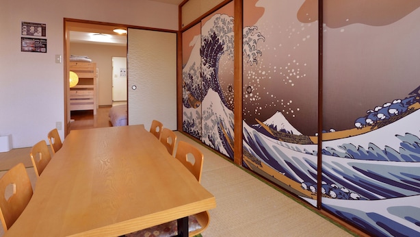 A traditional Japanese room with tatami flooring, a wooden table, and shoji screens with a wave painting. - Hostel Inn Tokyo Kuramae (Tokyo)