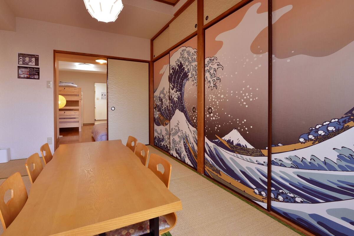 A traditional Japanese room with tatami flooring, a wooden table, and shoji screens with a wave painting.