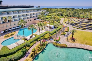 Un resort con varias piscinas, palmeras y un edificio grande con balcones.