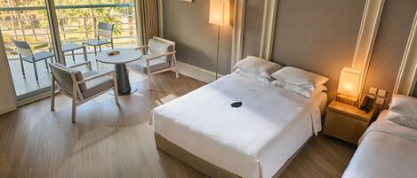 Habitación de hotel con una cama grande, un escritorio con una silla, una mesita pequeña y un balcón con sillas.