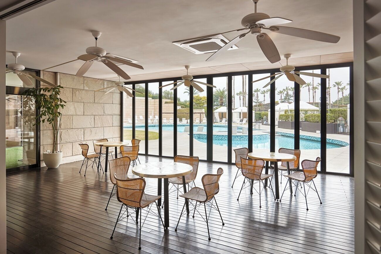 A spacious indoor area with multiple ceiling fans, large windows, and a view of an outdoor swimming pool.