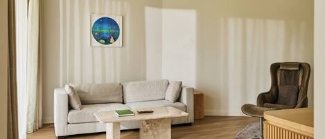 A modern living room with a beige sofa, a wooden coffee table, a framed picture on the wall, and a brown leather chair.
