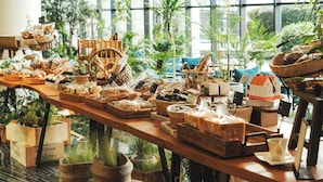 A wooden table filled with various food items and baskets, set in a room with large windows and indoor plants. - Grand Josun Jeju (Seogwipo)