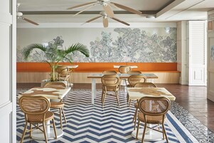 Un comedor con una mesa larga, sillas de mimbre y una alfombra estampada.