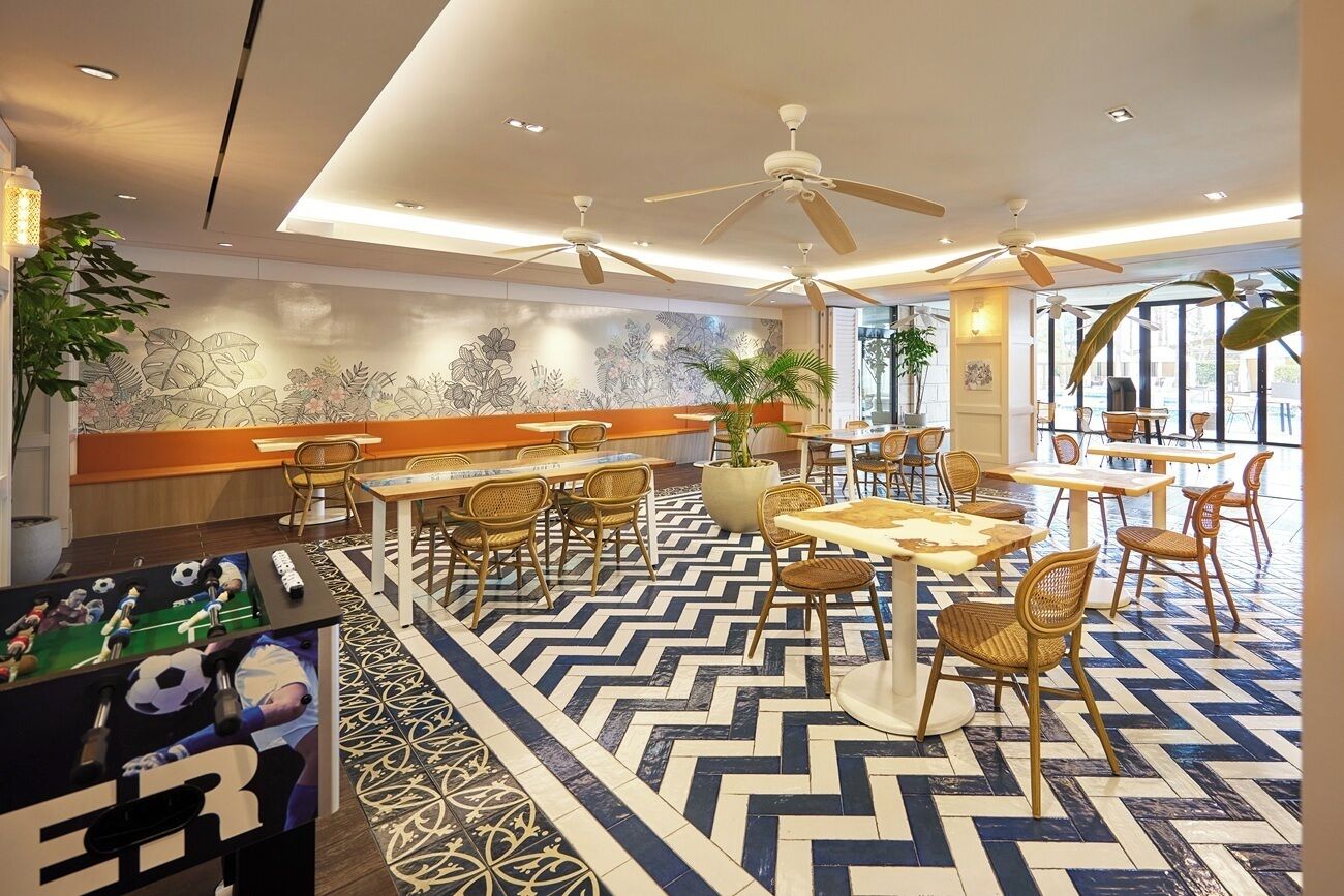 A modern indoor dining area with multiple tables and chairs, ceiling fans, and a decorative wall mural.