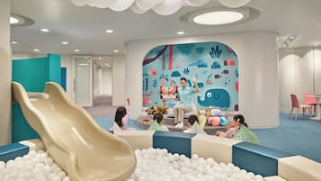Zona de juegos infantiles con tobogán, piscina de pelotas y un mural colorido.