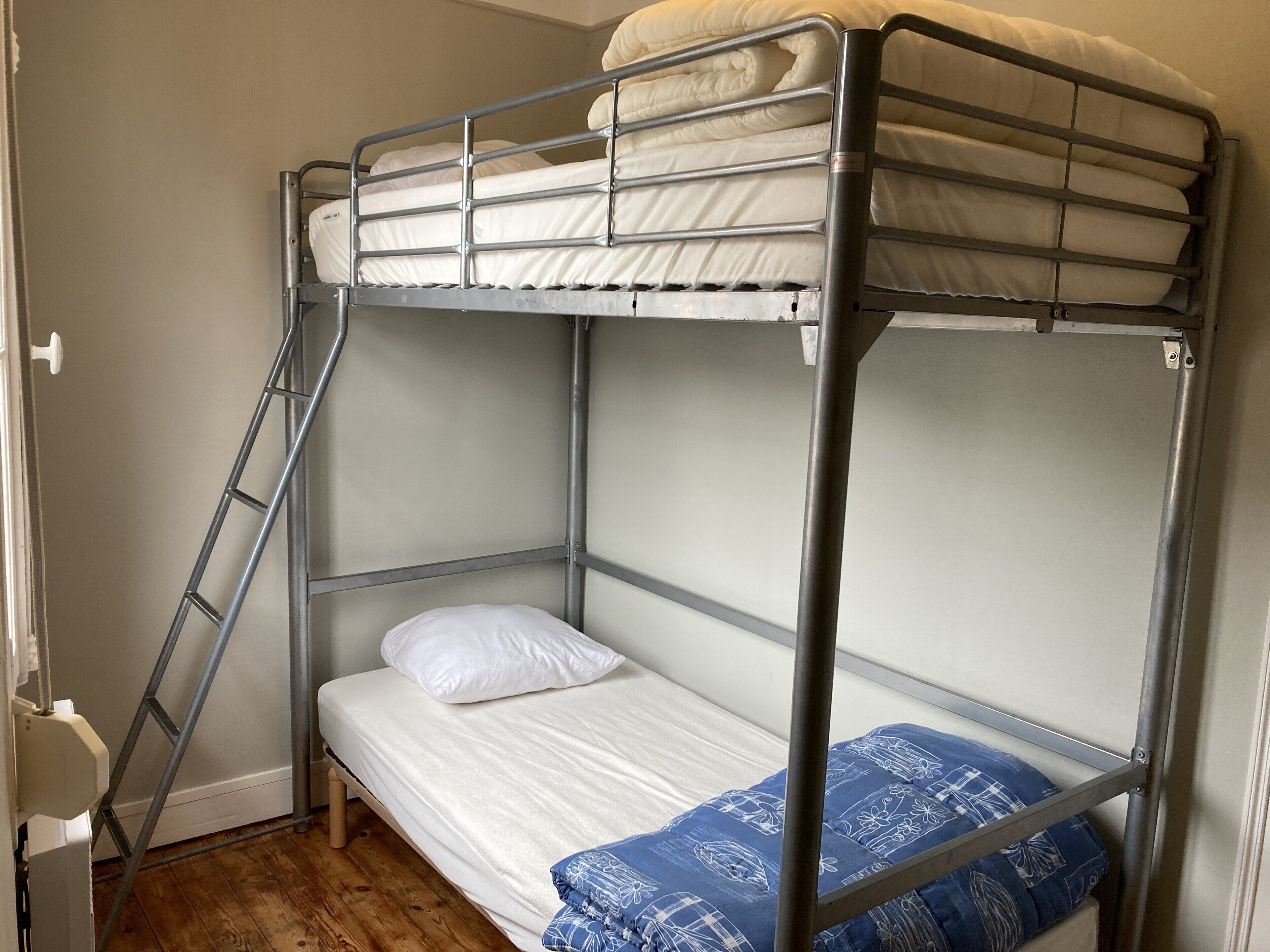 Una cama litera con escalera, una cama individual abajo y una almohada azul estampada.