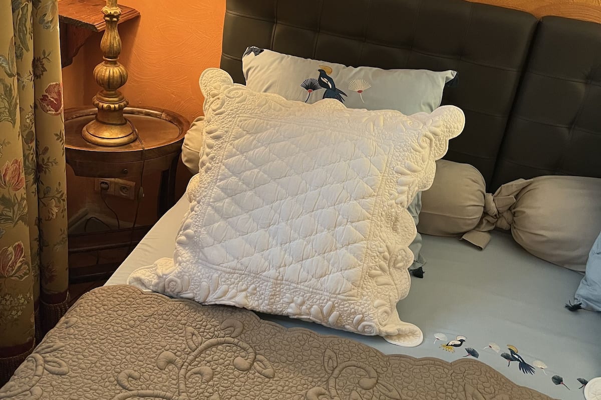 A neatly made bed with a quilted cover, a bedside lamp, and a framed picture on the wall.