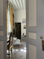 Una habitación de diseño clásico, con una silla de madera con estampado floral, una puerta blanca con tirador de latón y una ventana con cortinas amarillas.