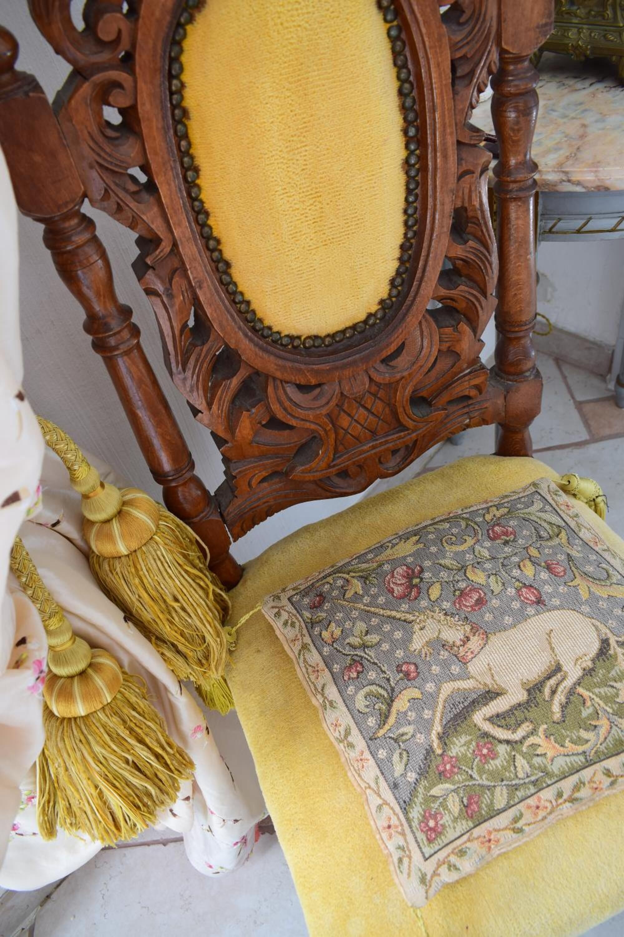 A wooden chair with a yellow cushion and a decorative pillow with floral embroidery.