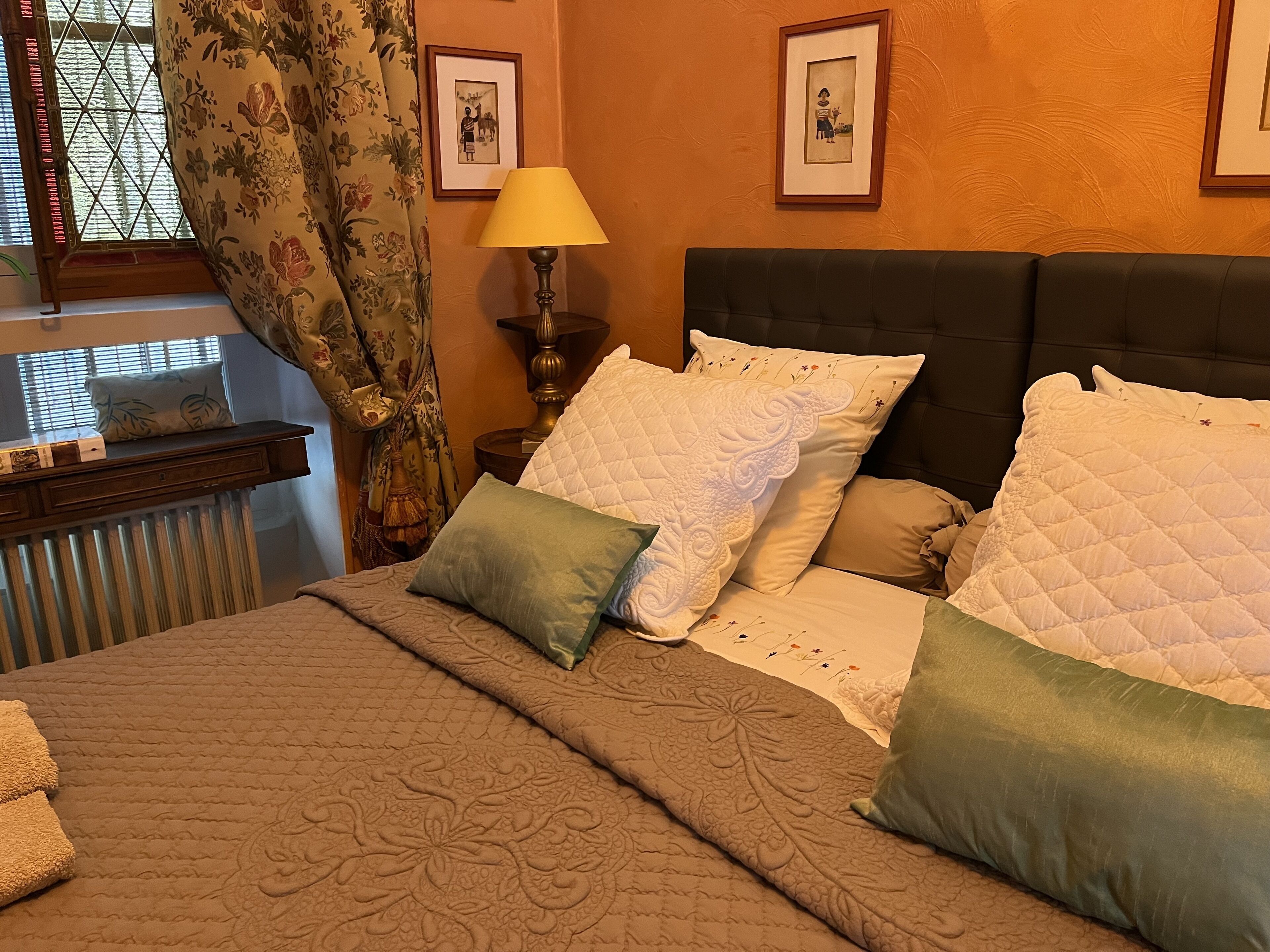 Ein Schlafzimmer mit einem Bett, Kissen, einem Nachttisch, einer Lampe und gerahmten Bildern an der Wand.