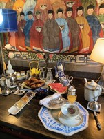 Una mesa de comedor con un juego de té chino tradicional, pasteles y un cuadro decorativo al fondo.