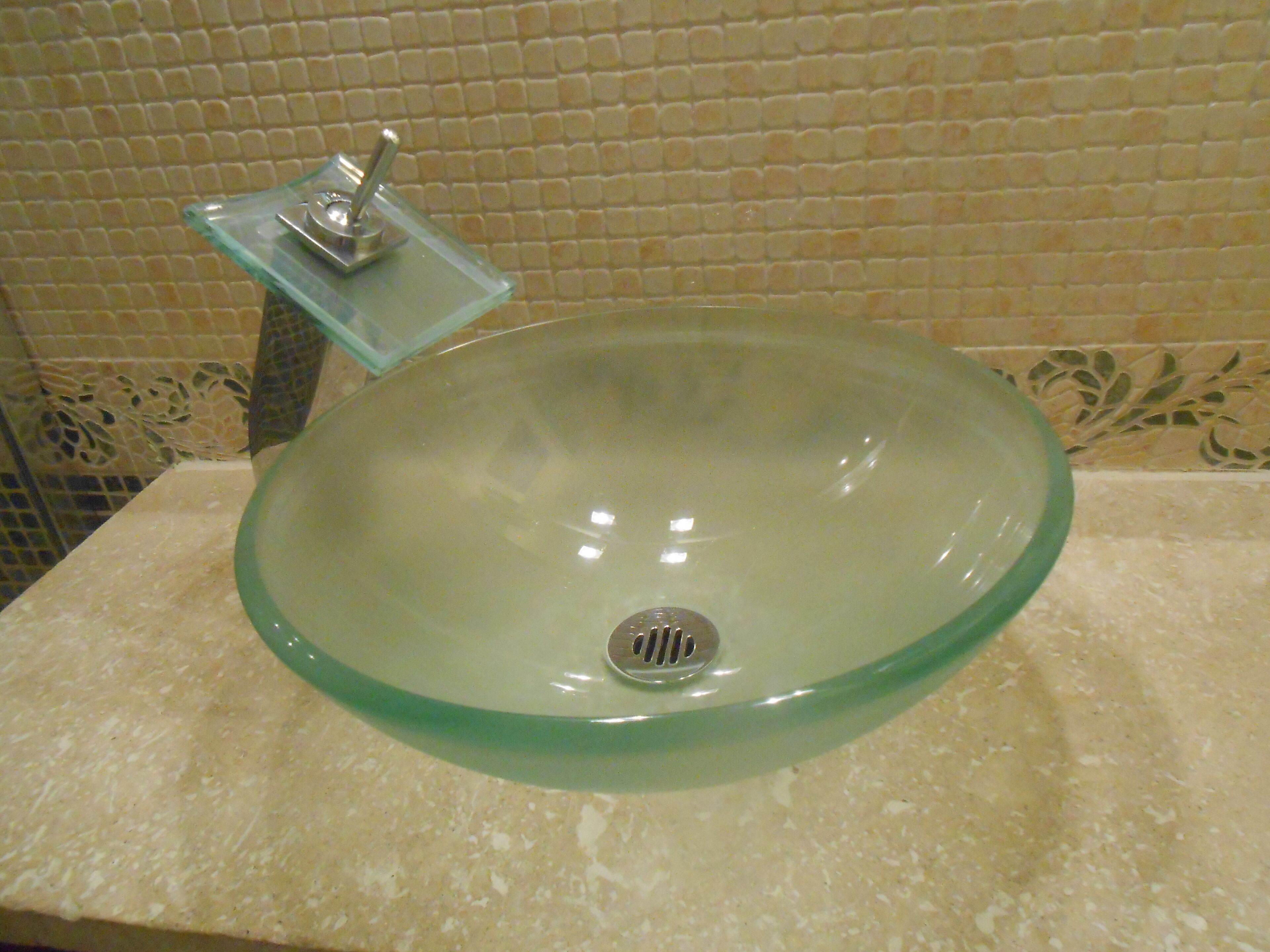 Une salle de bain avec un lavabo en verre, un porte-savon en verre et un mur recouvert de carreaux.