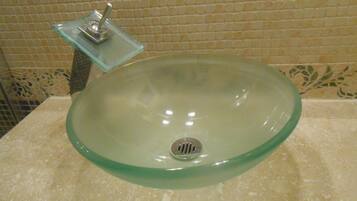 Une salle de bain avec un lavabo en verre, un porte-savon en verre et un mur recouvert de carreaux.
