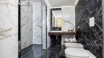 Un baño moderno con cabina de ducha de vidrio, inodoro blanco y tocador de mármol.