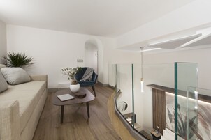 Una sala de estar moderna con sofá, una mesita de centro, una silla azul y barandilla de vidrio.