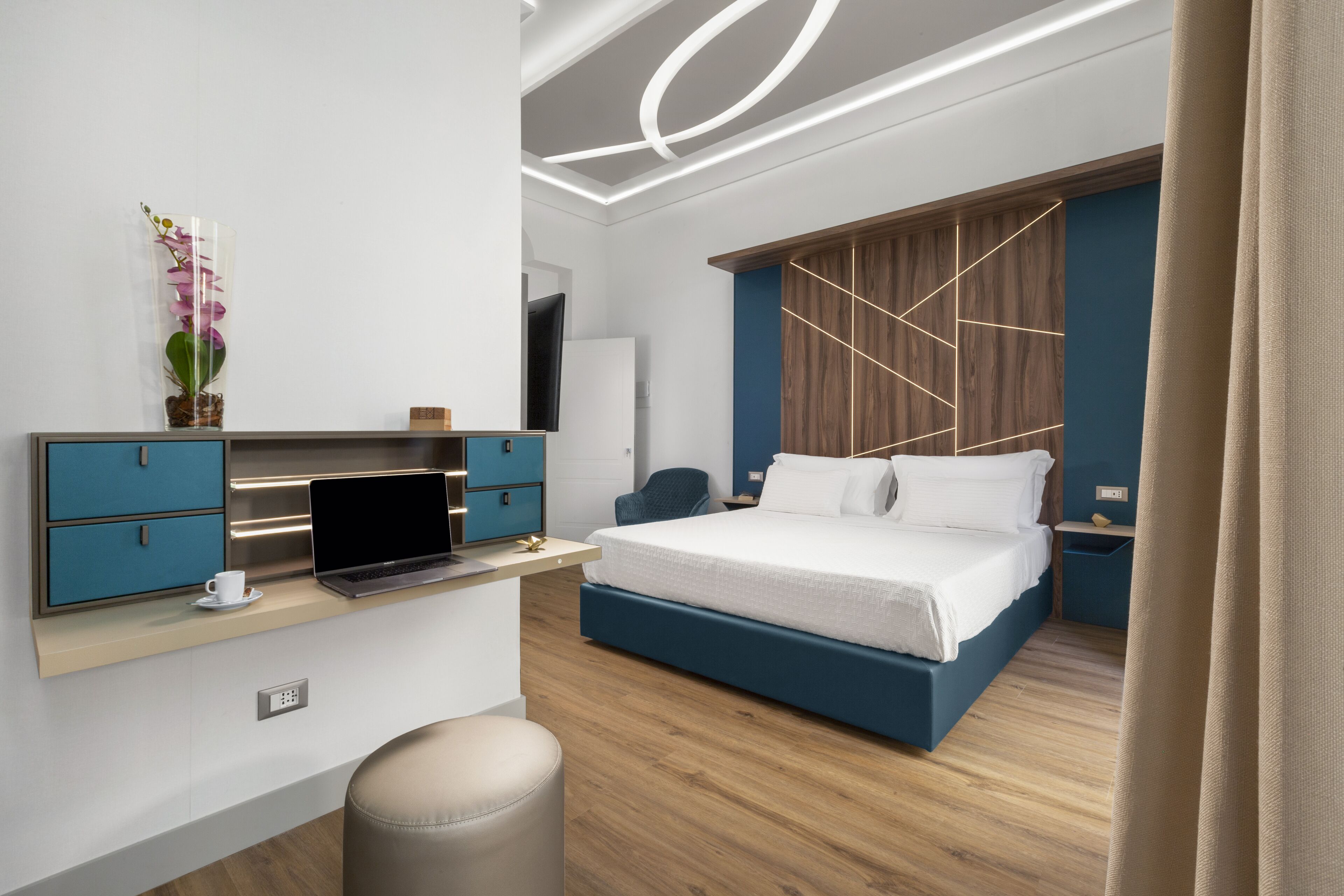 Quarto moderno com cama, escrivaninha com laptop, cadeira e uma pequena mesa com uma xícara.