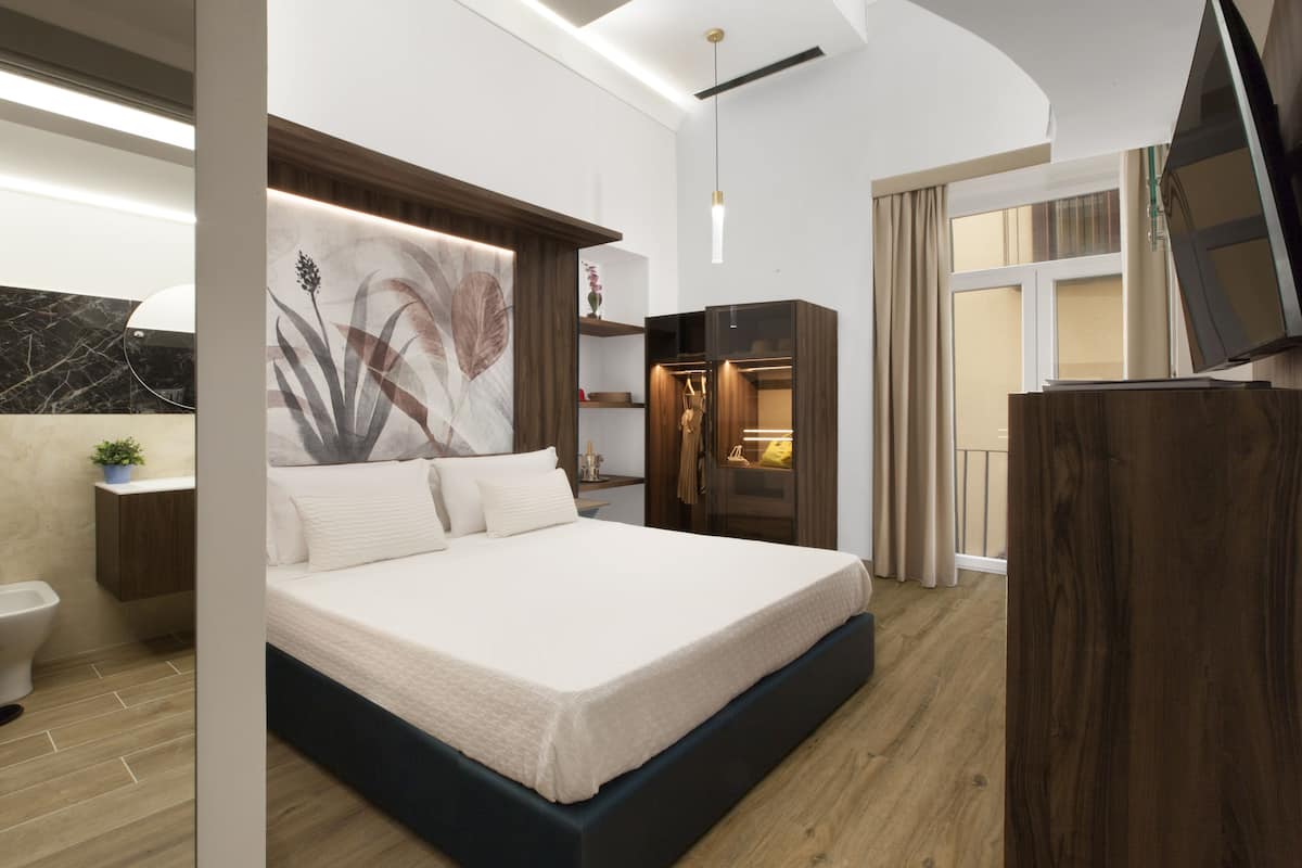 A modern bedroom with a large bed, a wardrobe, a TV, and a bathroom with a toilet and sink.
