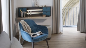 A modern living room with a blue armchair, a wooden floor, a built-in TV shelf, and a view of a balcony. - Elys Suites (Sorrento)