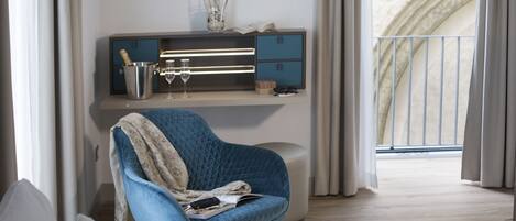 A modern living room with a blue armchair, a wooden floor, a built-in TV shelf, and a view of a balcony.