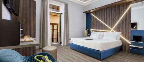 A modern hotel room with a bed, a seating area, a TV, and a wardrobe.