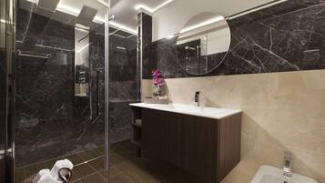 Une salle de bain moderne avec une douche à parois de verre, un mur recouvert de carreaux de marbre, un meuble-lavabo en bois et un lavabo blanc.