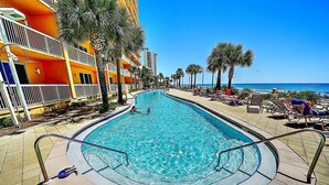 A swimming pool with a 3 FT no diving sign, surrounded by palm trees and lounge chairs, with a building in the background.