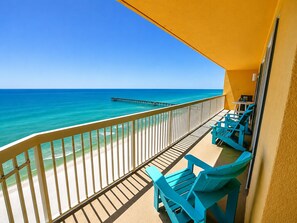 A balcony with a view of the ocean and a pier, featuring turquoise chairs and a yellow wall.
