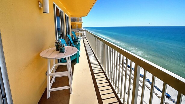 A balcony with a table and chairs, overlooking a beach with umbrellas and lounge chairs.