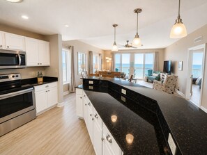 A modern kitchen with a black granite countertop, stainless steel appliances, and a dining area with a view of the ocean.