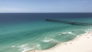 A beach with a pier extending into the ocean, clear skies, and calm waters.