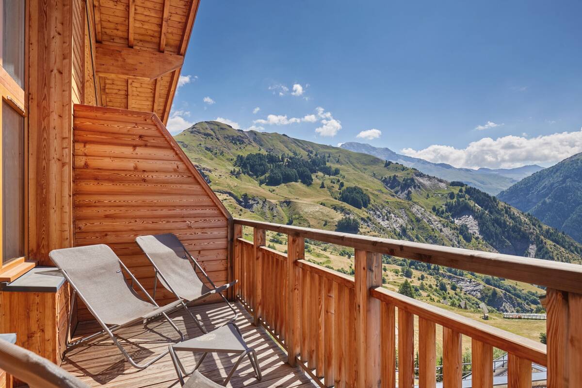 A wooden balcony with two lounge chairs overlooking a mountainous landscape.