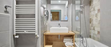Een moderne badkamer met een witte wasbak, houten wastafelmeubel, handdoekrek en een douchegedeelte.