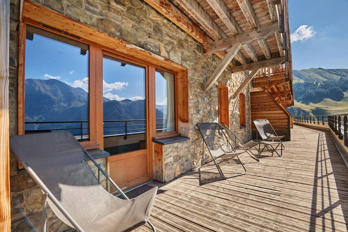 A wooden deck with two lounge chairs, a stone wall, and a view of mountains.
