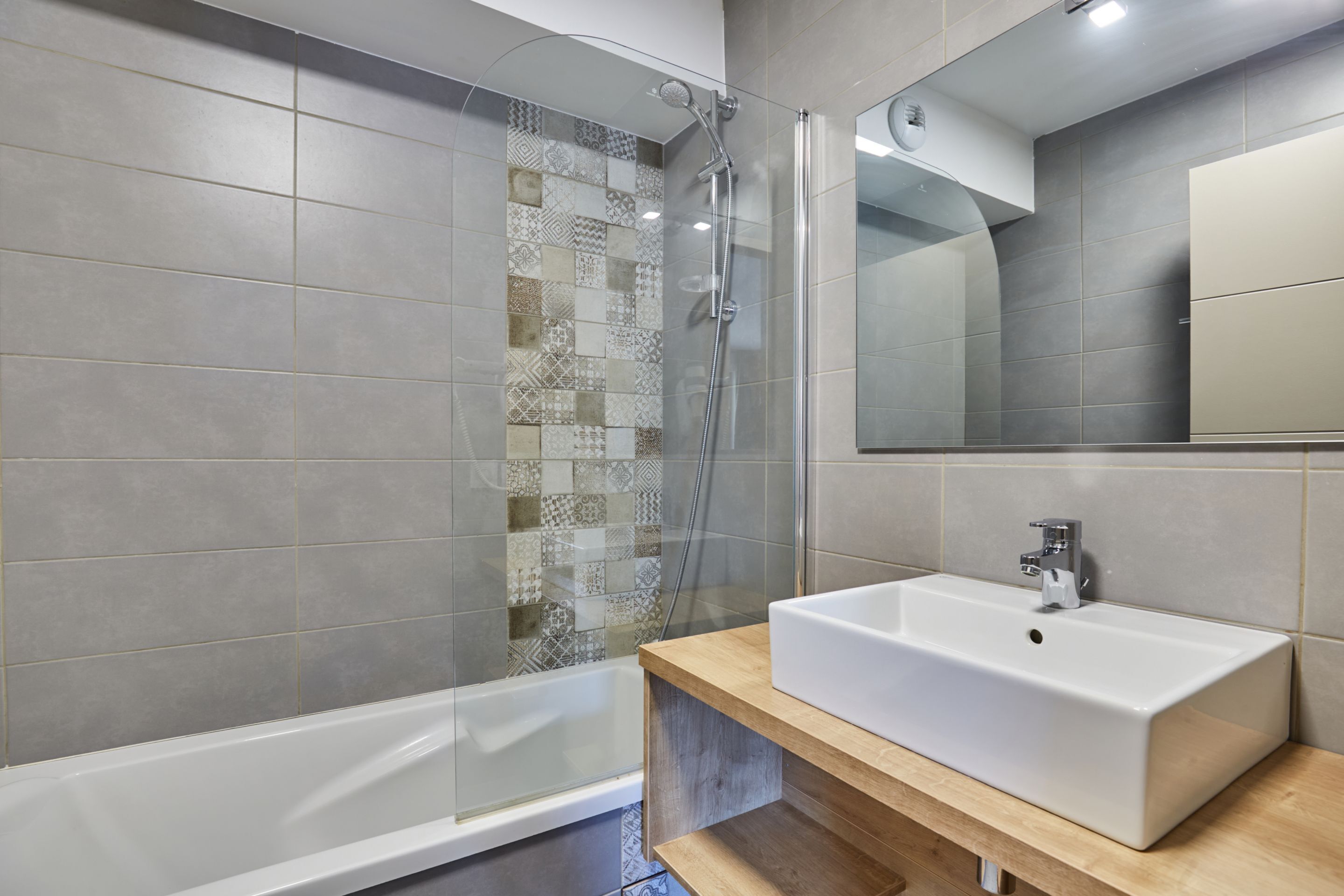 Une salle de bain moderne avec une grande douche, un lavabo blanc et un mur recouvert de carreaux à motifs.