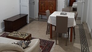 Una sala de estar con un sofá, una mesa de comedor con sillas, un televisor sobre un mueble y una alfombra estampada.