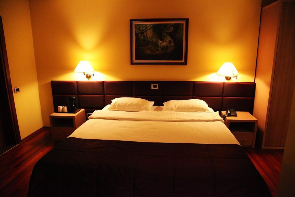 Habitació d'hotel amb un llit gran, dues taules de nit, una tauleta auxiliar, un quadre a la paret i dues làmpades de paret.