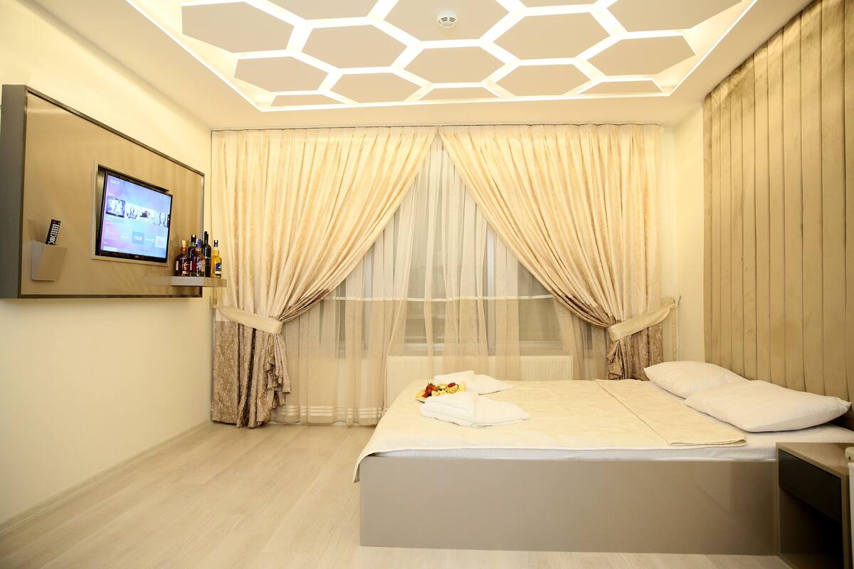 Una habitación de hotel moderna con una cama grande, un televisor en la pared y un plafón con lámpara de diseño geométrico.