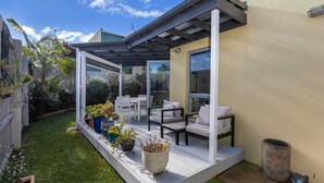Une terrasse couverte avec des meubles d’extérieur, un petit jardin et une vue sur les environs.