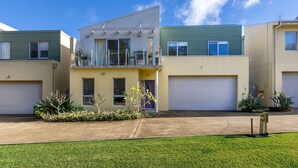 Un immeuble résidentiel moderne à deux étages, doté d’un balcon, d’un garage et d’une pelouse bien entretenue.